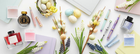 Spring pastel colors of fountain pens, ink, and notebooks with flowers and speckled eggs